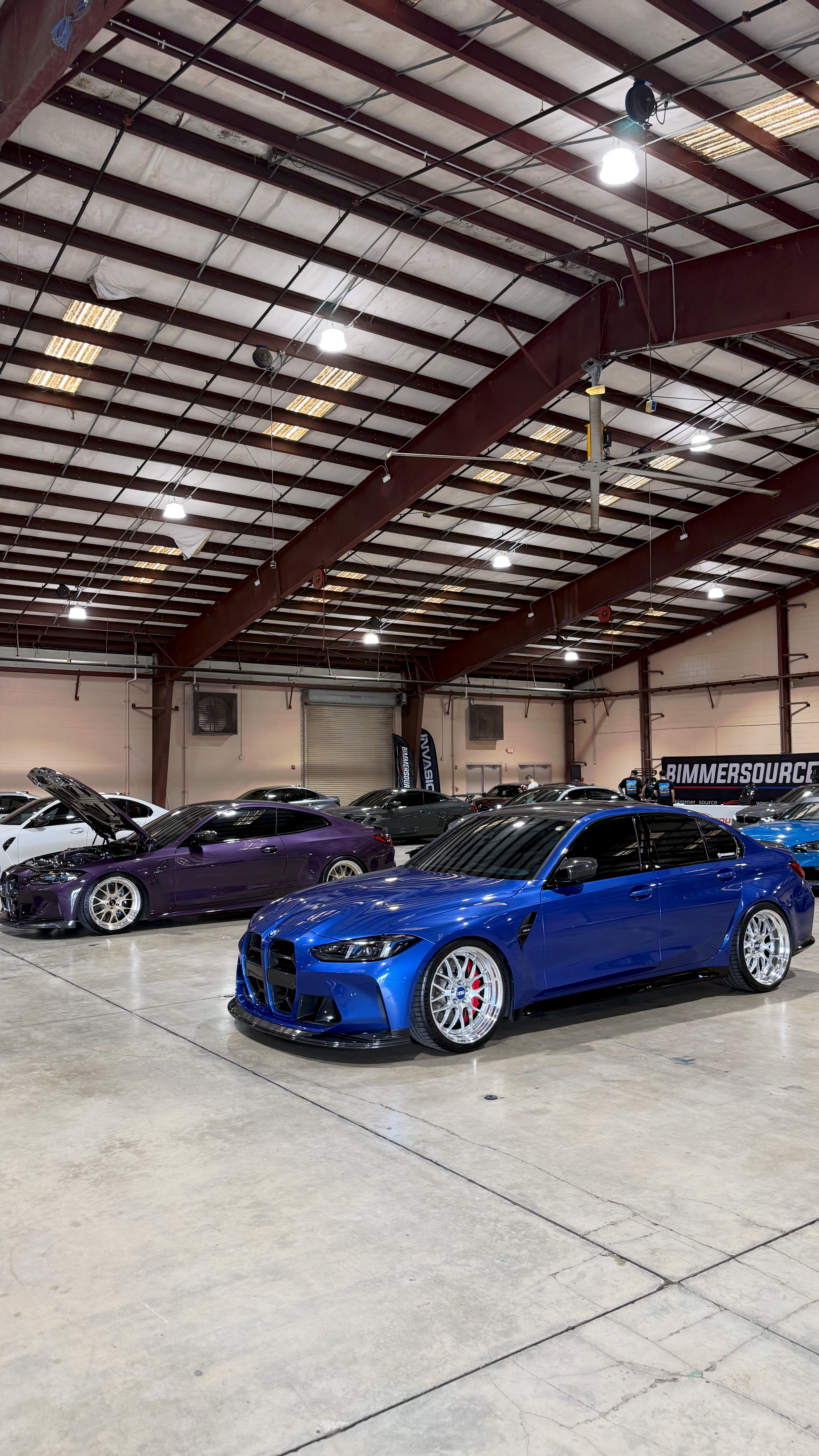 Blue BMW G80 M3 with carbon aero and a silver M3 at a Shell station at dusk