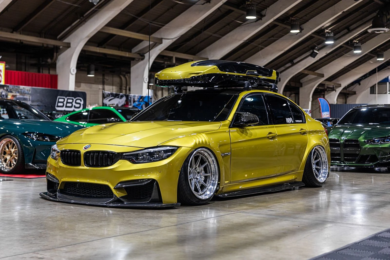 Yellow BMW F80 M3 with a roof box and carbon aero at an indoor car show